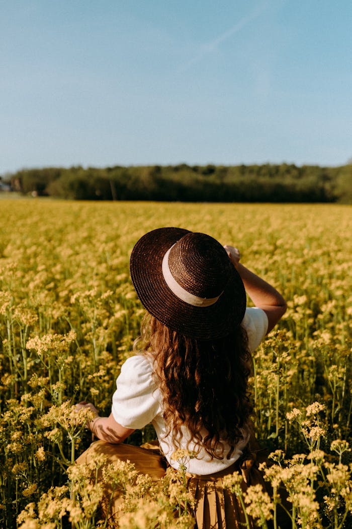 A woman with a hat enjoys a sunny spring day in a blooming canola field.